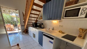 A compact kitchen with white cabinets, a microwave, a sink, and a trash bin.