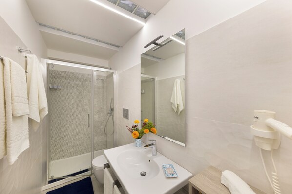 Un baño moderno con cabina de ducha de vidrio, un lavabo blanco con un florero y un espejo sobre el lavabo.