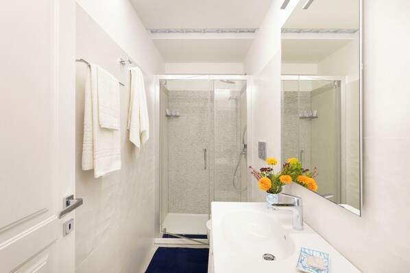 A bathroom with a shower, a sink, a mirror, and towels on a rack. - YourHome - Royal Blue Suite (Sorrento)