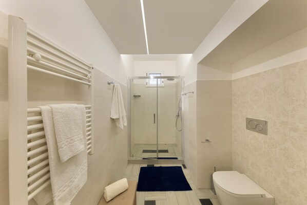 Une salle de bain moderne avec une douche à parois de verre, des toilettes blanches et un porte-serviettes avec des serviettes.