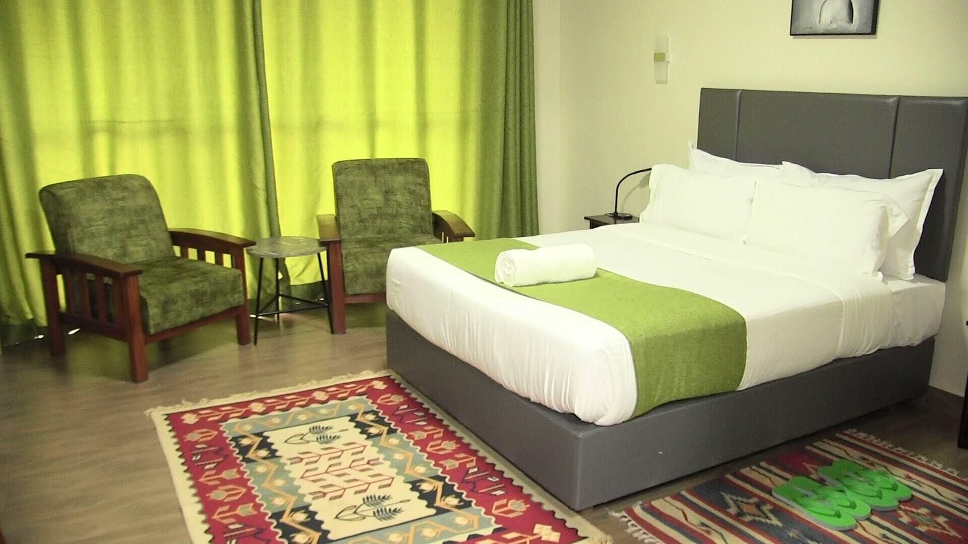 Een hotelkamer met een bed, twee stoelen, een klein tafeltje en een kamerkleed met een patroon.