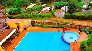 A swimming pool with a circular deck area, surrounded by a brick wall and a green fence.