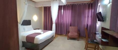A bedroom with a bed, a chair, a desk, and a TV.