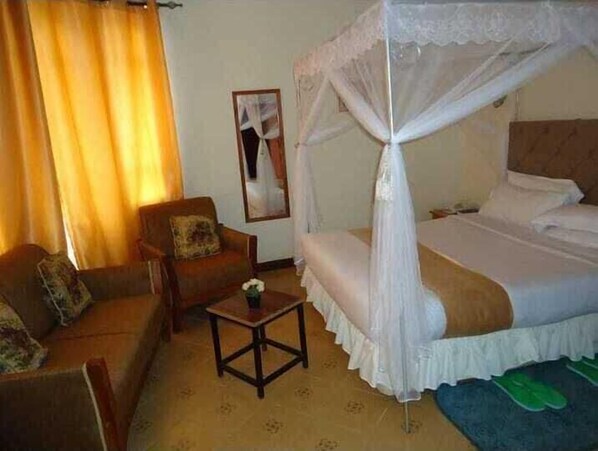 A bedroom with a four-poster bed, a sofa, a small table, and a mirror on the wall. - Westside Hotel Kitale (Kitale)