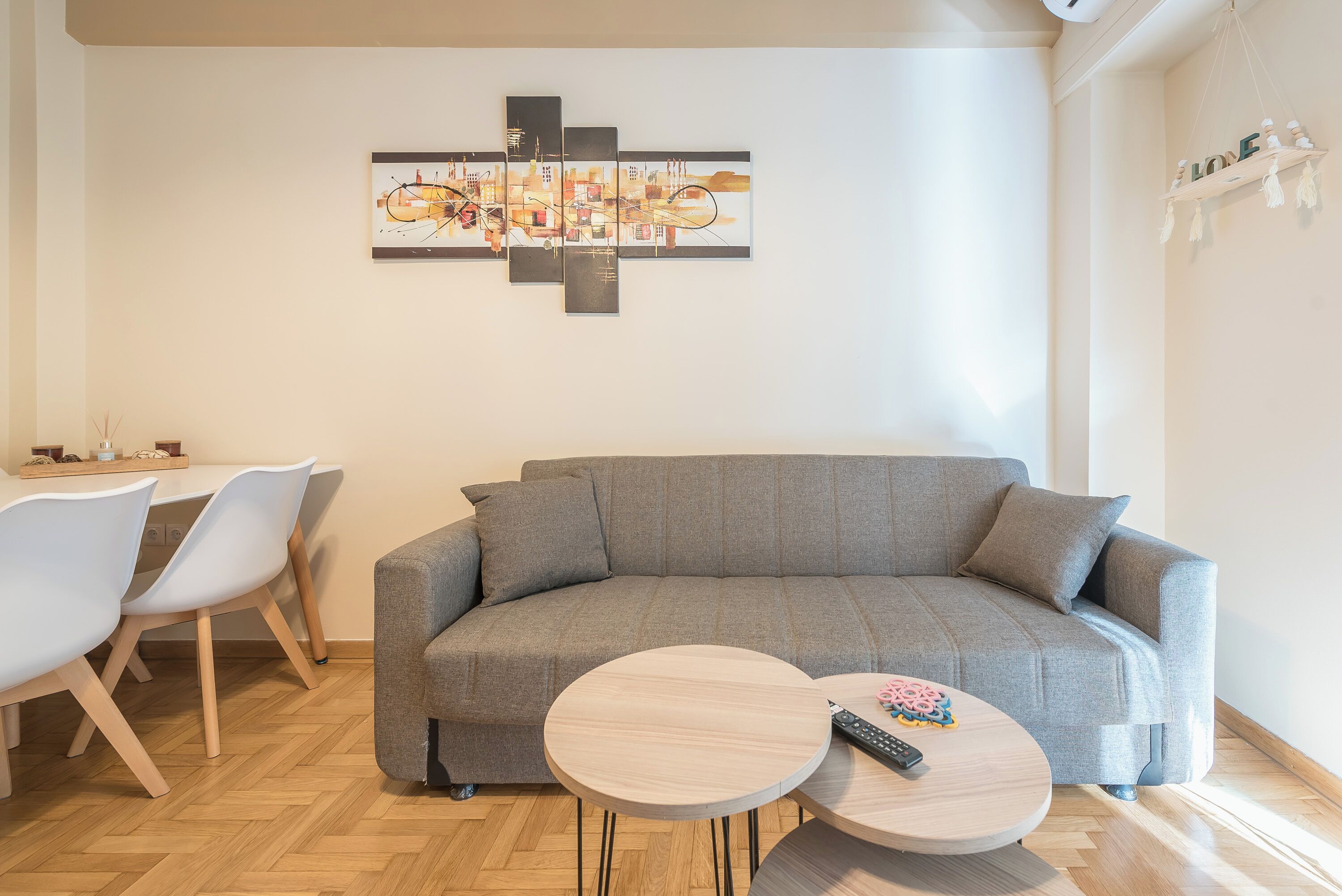 A modern living room with a grey sofa, two round coffee tables, and a dining area with white chairs.