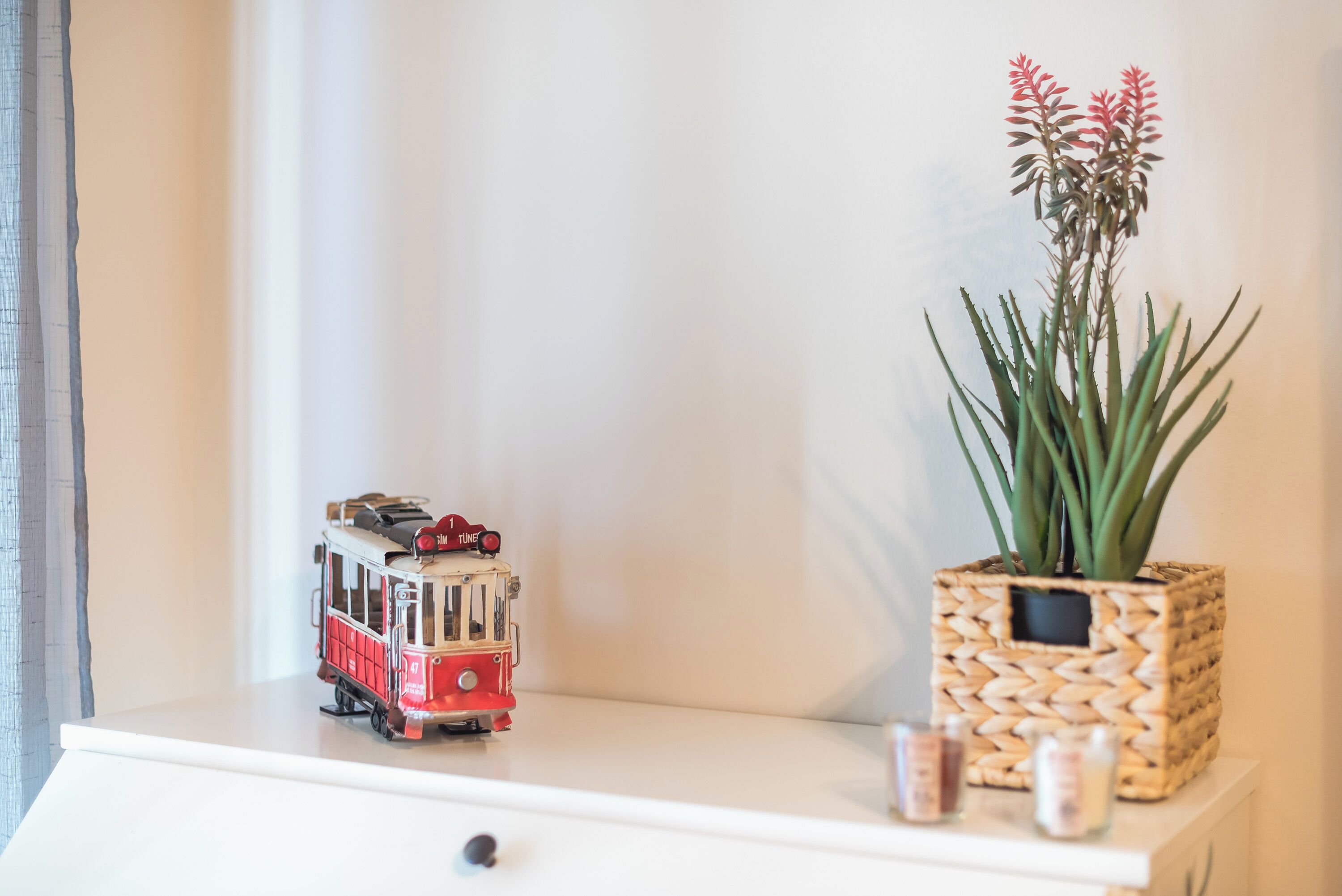 Un petit train jouet sur une commode blanche, une plante en pot et quelques bougies.
