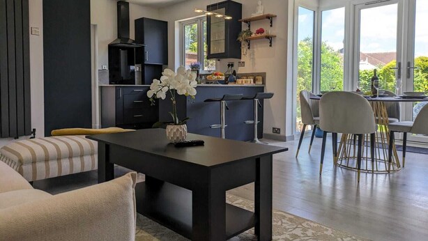Una cocina moderna con armarios oscuros, una isla central y un comedor con mesa y sillas.