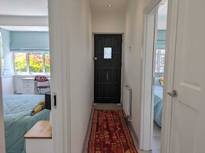 A narrow hallway with a dark door, a patterned rug, and a bed with a blue bedspread. - Cozy Cottage Stay - Modern, Cozy, Close to London (Epsom)