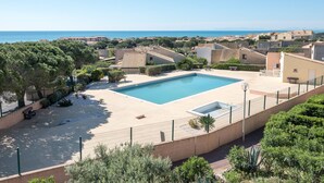 A swimming pool surrounded by a fence, with a view of the sea and buildings in the background. - T2 Mezzanine Villa - Air Conditioning - Veranda - Parking - Pool - 6 People (Fleury-Saint-Pierre-la-Mer)