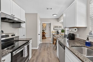 A modern kitchen with stainless steel appliances, a granite countertop, and a coffee bar area. - Hot Tub+Beach Volleyball+Fire pit+Movie Room+More! (pooler)