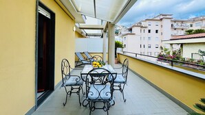 Un balcon avec une table et des chaises, une plante en pot et une vue sur les bâtiments en arrière-plan.