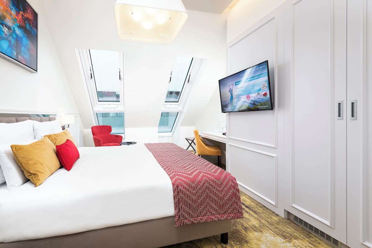 Ein modernes Hotelzimmer mit Bett, Schreibtisch, Sessel, Fernseher und großem Fenster.