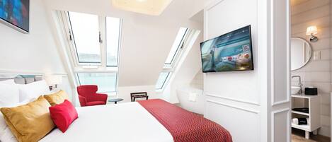 Une chambre d’hôtel moderne avec un grand lit, des oreillers rouges et dorés, un téléviseur fixé au mur et un fauteuil rouge.