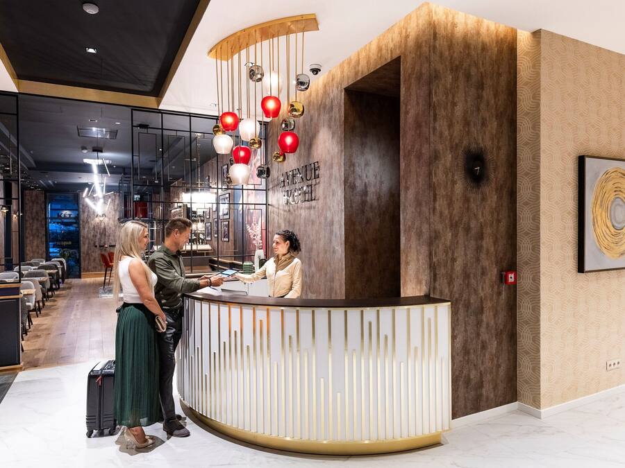 Una moderna zona de recepción de hotel con un mostrador de madera, un reloj digital y un papel tapiz decorativo.