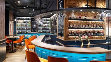 A bar area with a curved counter, orange chairs, and shelves stocked with bottles and glasses.