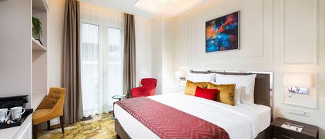 Habitación de hotel con una cama grande, una silla roja, un escritorio con cafetera y un cuadro en la pared.