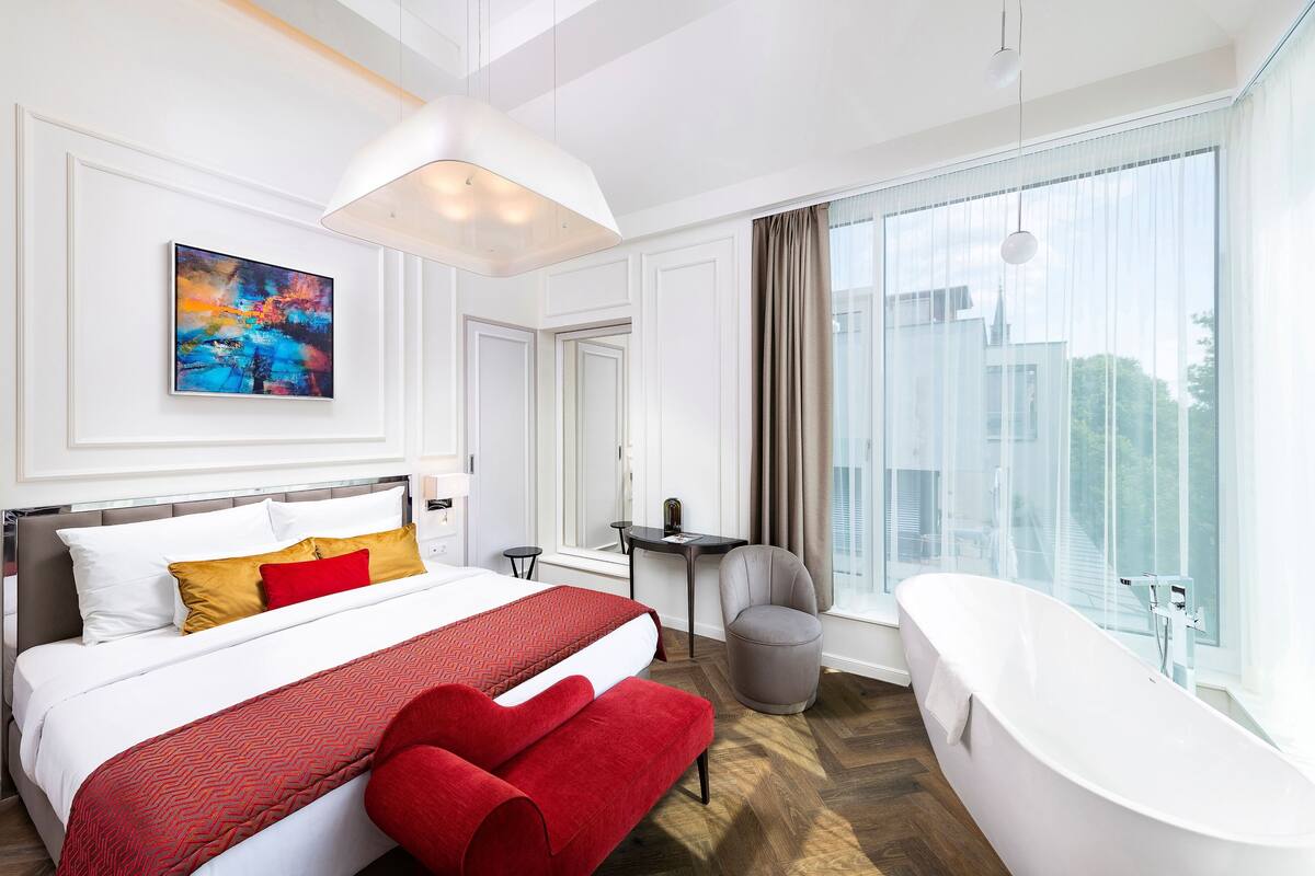 Ein modernes Hotelzimmer mit einem großen Bett, einer Sitzecke, einer Badewanne und Blick auf die Stadt.