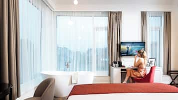 Una habitación de hotel moderna con una cama grande, una zona de estar con escritorio, una bañera y un televisor que muestra un mensaje de bienvenida.