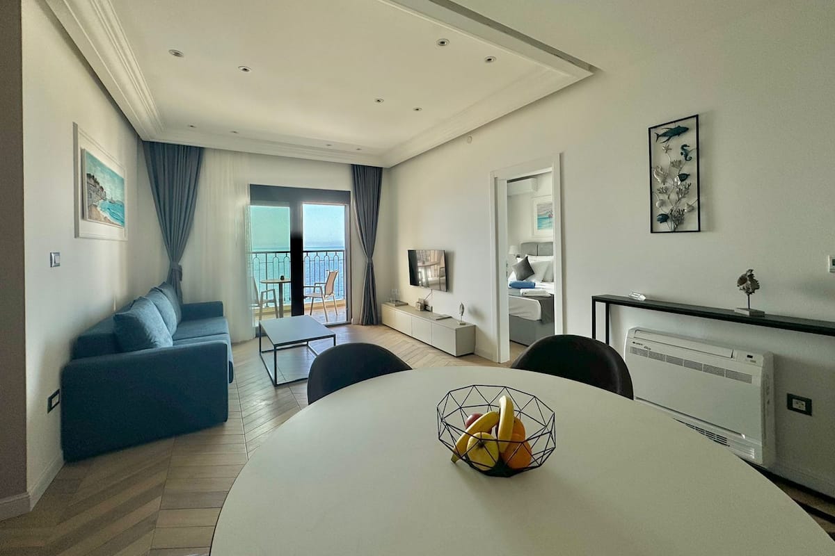 A modern living room with a balcony, a dining area, and a bedroom with a view.