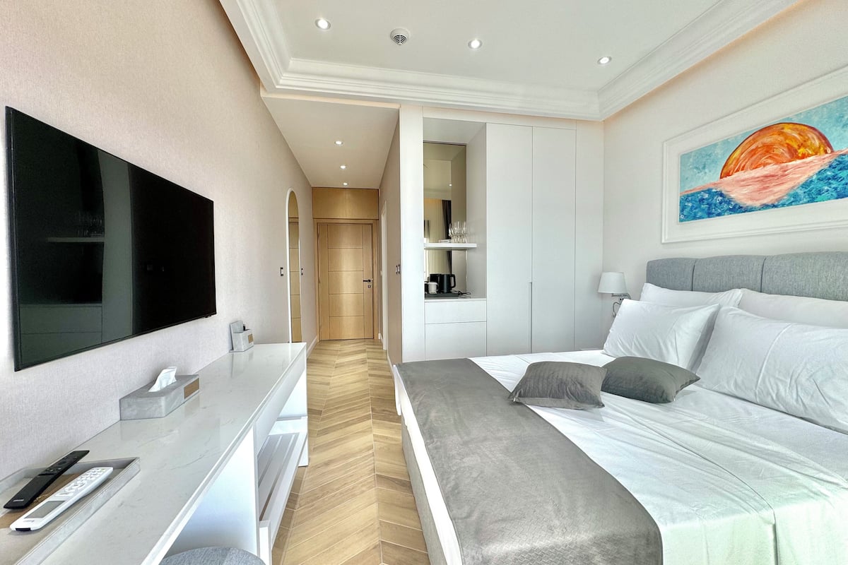 A modern hotel room with a large bed, a flat-screen TV, a desk with a computer, and a painting on the wall.
