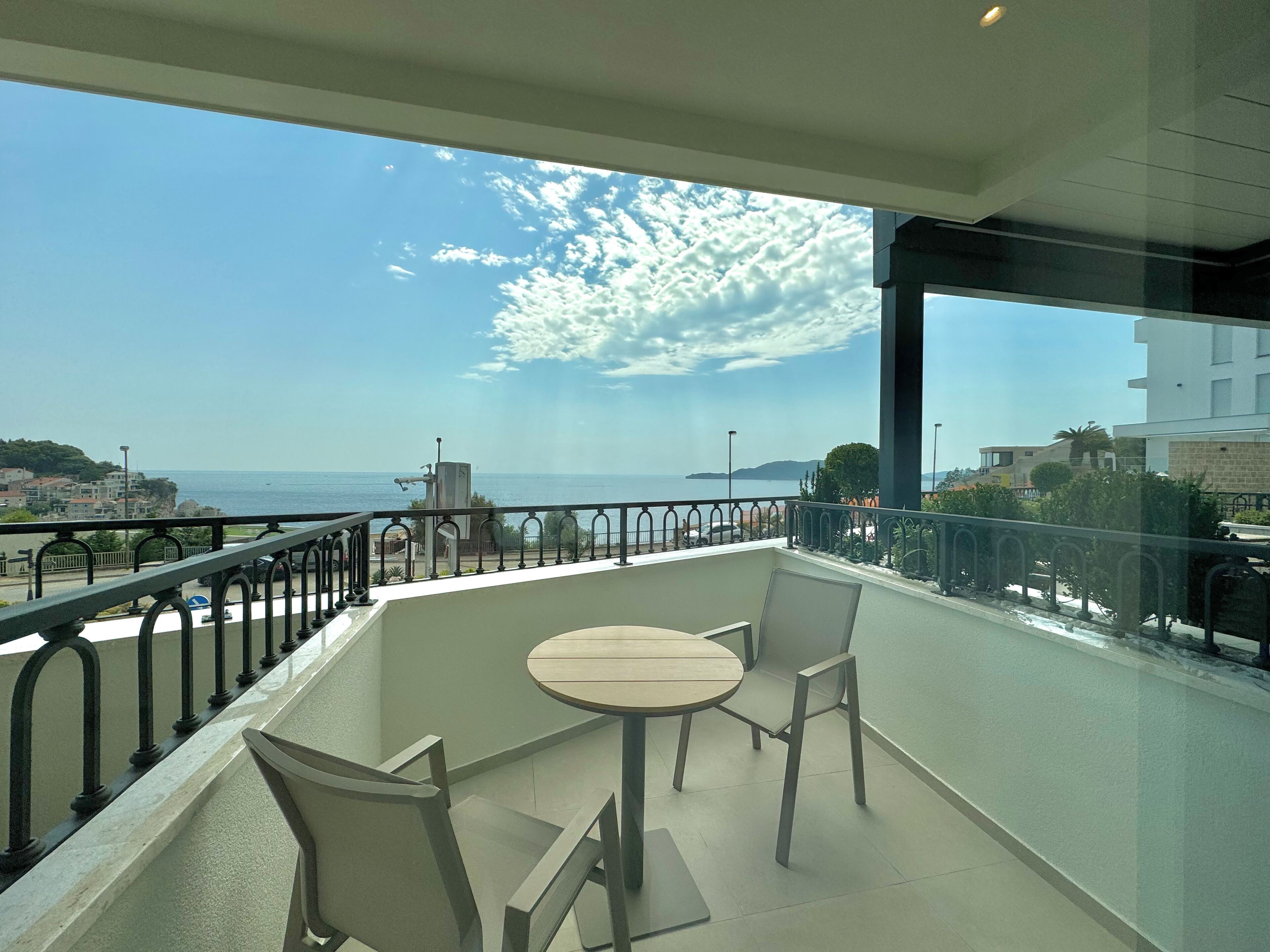 Un balcón con mesa y sillas, con vistas a la costa, edificios y un cielo despejado.