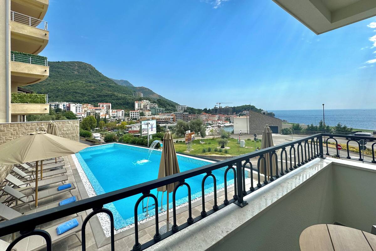 A balcony with a pool, overlooking a coastal town and mountains.
