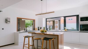 Eine moderne Küche mit einer zentralen Kochinsel, zwei Barhocker, einem großen Fenster und einem Backofen.