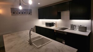 A modern kitchen with a marble countertop, black cabinets, and a unique rope light fixture.