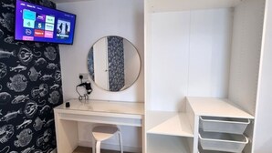 A bedroom with a bed, a desk, a chair, a wardrobe, a mirror, and a TV on the wall.