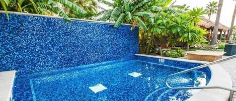 Una piscina con diseño de mosaicos, rodeada de plantas tropicales y una palmera.