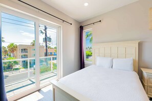 A hotel room with a large bed, a window with a view of the street, and a balcony. - Amberjack Oasis (South Padre Island)