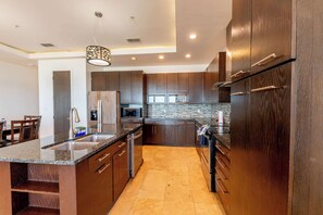 A modern kitchen with dark wood cabinets, granite countertops, stainless steel appliances, and a central island. - Amberjack Oasis (South Padre Island)