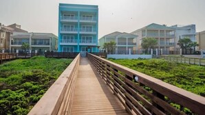 A wooden boardwalk leading to a modern building with multiple balconies. - Amberjack Oasis  (South Padre Island)