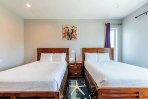 A hotel room with two beds, a starfish rug, a nightstand, and a painting on the wall.