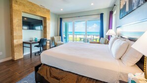 A hotel room with a large bed, a desk, a chair, and a view of the ocean. - Amberjack Oasis  (South Padre Island)