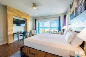 A hotel room with a large bed, a desk, a chair, and a view of the ocean. - Amberjack Oasis  (South Padre Island)