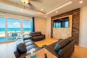 A modern living room with leather sofas, a flat-screen TV, and a view of the beach. - Marlin Cove (South Padre Island)