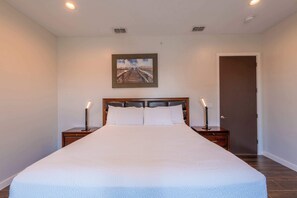 A bedroom with a large bed, two bedside tables, a door, and a painting on the wall.
