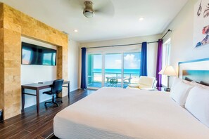 A hotel room with a large bed, a desk with a chair, a TV mounted on a stone wall, and a balcony with a view of the sea. - Marlin Cove (South Padre Island)