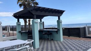 Une terrasse extérieure équipée d’un barbecue, de sièges et offrant une vue sur l’océan.