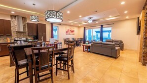 Een moderne keuken met donkere houten kastjes, een centraal eiland met stoelen, en een zithoek met een grijze bank en tafel.