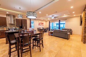 A modern kitchen with dark wooden cabinets, a central island with chairs, and a dining area with a gray sofa and table.