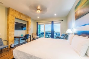 A hotel room with a large bed, a desk with a chair, a TV, and a balcony with a view. - Starfish Sanctuary  (South Padre Island)