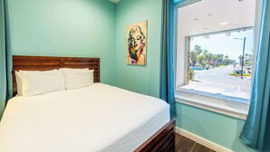 Een slaapkamer met een bed, een raam met uitzicht op de straat en een schilderij aan de muur.