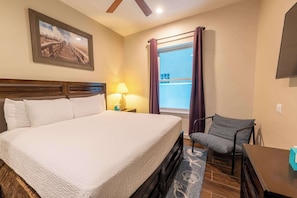 Une chambre d’hôtel avec un grand lit, une chaise, un bureau, une lampe, une fenêtre avec des rideaux et un tableau au mur.