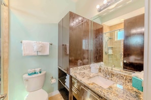 A bathroom with a toilet, a sink with a marble countertop, a mirror, and a shower area. - Dolphin Paradise (South Padre Island)