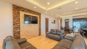 A modern living room with a stone accent wall, a flat-screen TV, leather sofas, and a dining area with wooden furniture. - Dolphin Paradise  (South Padre Island)