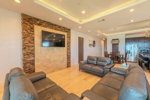 A modern living room with a stone accent wall, a flat-screen TV, leather sofas, and a dining area with wooden furniture.