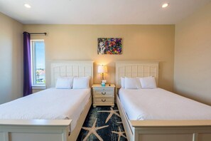 A hotel room with two beds, a star-patterned rug, a nightstand with a lamp, and a painting on the wall.