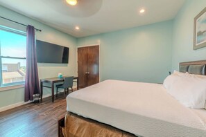 A hotel room with a large bed, a desk, a chair, a TV mounted on the wall, and a window with curtains.